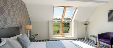 Un dormitorio con una cama grande, vistas a un campo de golf a través de un tragaluz, una lámpara moderna y una silla morada.