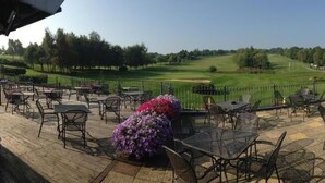 An outdoor patio with tables and chairs, a golf course in the background, and a building with windows. - Wharton Park Golf & Country Club (Bewdley)
