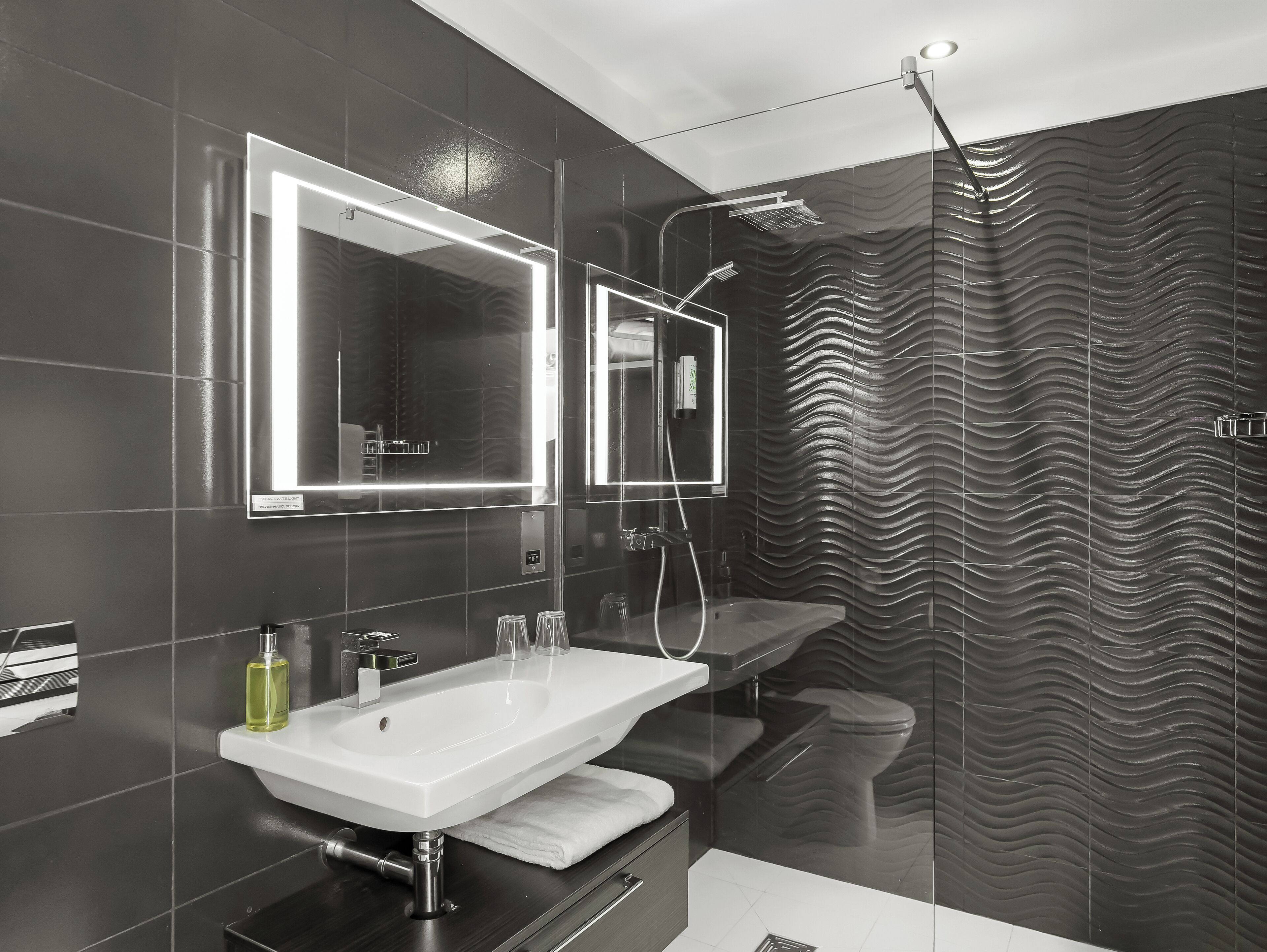 A modern bathroom with a large mirror, a sink, and a shower.