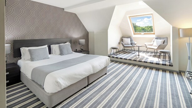 A modern bedroom with a large bed, a desk, two chairs, and a skylight. - Wharton Park Golf & Country Club (Bewdley)