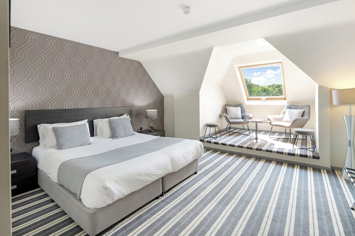 A modern bedroom with a large bed, a desk, two chairs, and a skylight.