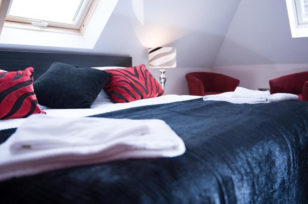 A modern hotel room with a neatly made bed, a red chair, and a lamp.