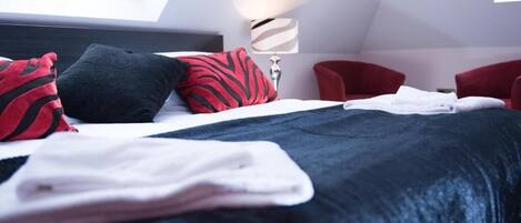 A modern hotel room with a neatly made bed, a red chair, and a lamp.
