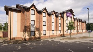 A row of brick buildings with a prominent 'Premier Inn' sign, a parking lot, and a clear sky. - Premier Inn Birmingham South - Rubery (Birmingham)