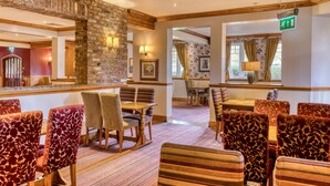 A hotel lobby with a stone wall, wooden beams, striped chairs, and a reception desk. - Premier Inn Birmingham South - Rubery (Birmingham)