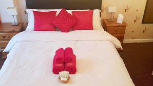 A neatly made bed with a white duvet, red pillows, and a pair of red slippers on the bed. - Oban House Hotel (Blackpool)