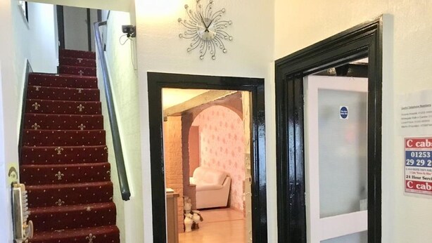 A staircase leading to a room with a white sofa, a small dog, and a clock on the wall. - Oban House Hotel (Blackpool)