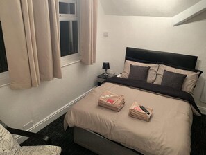 A neatly made bed with a black headboard, beige bedding, and two folded towels on the bed. - Oban House Hotel (Blackpool)