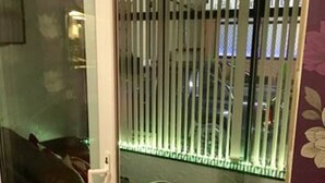 A room with a red leather sofa, a wicker ottoman, and a glass door leading to a balcony with vertical blinds. - Oban House Hotel (Blackpool)