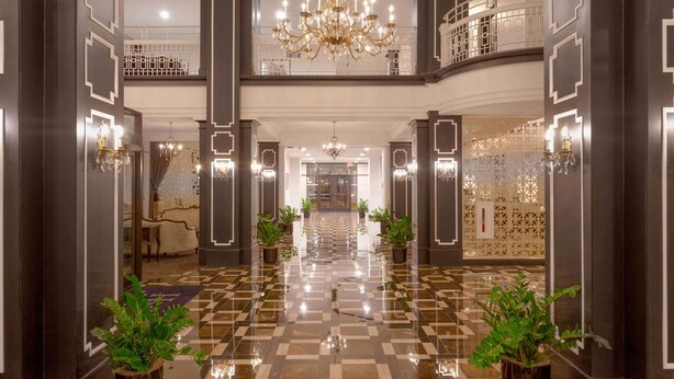 Un'imponente hall d'albergo con pavimento a scacchi, lampadari e piante in vaso.