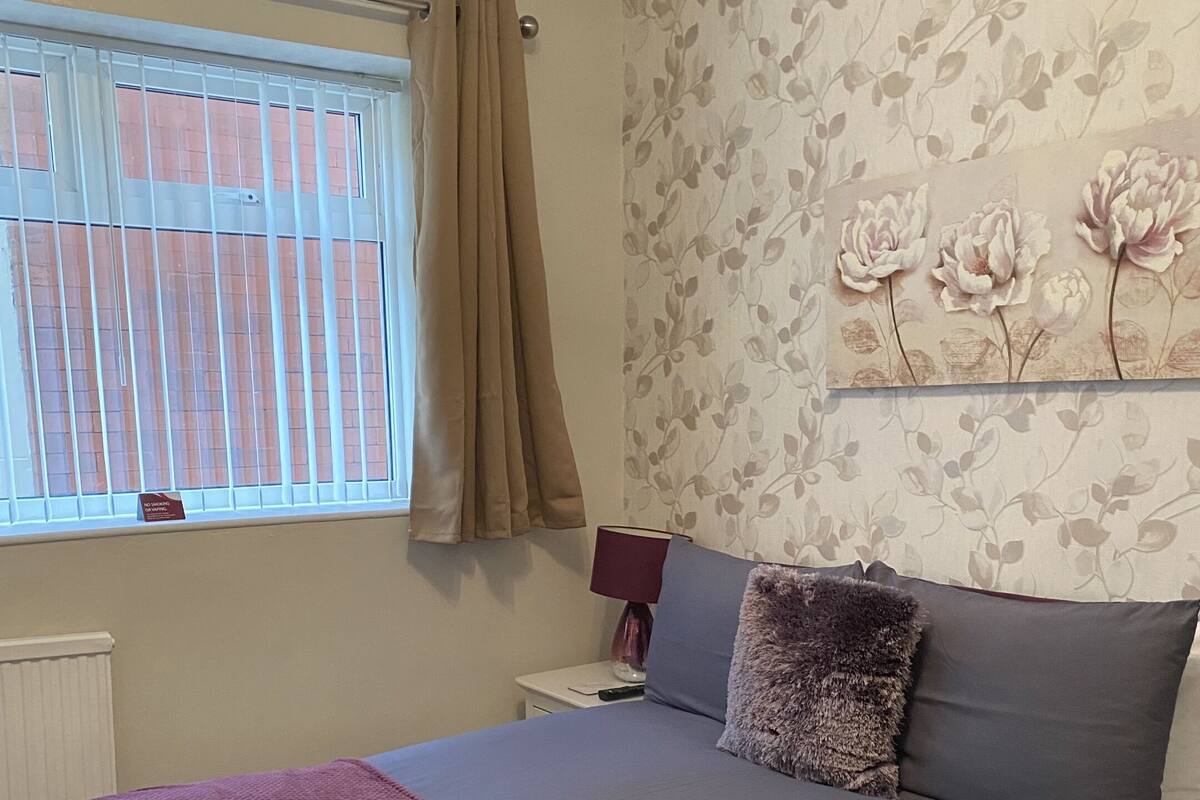 Une chambre à coucher avec un lit, une table de chevet, une fenêtre avec des rideaux et un papier peint à motifs floraux.