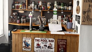 En bar med flasker på hylder, et skilt med teksten "The Pool Bar" og en velkomstskilt.