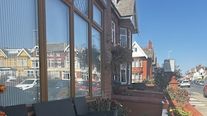 En terrasse med udendørs møbler, en velholdt græsplæne og udsigt til gaden og bygningerne i baggrunden.