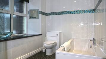 Un baño con inodoro, lavamanos de vidrio, bañera y zona de ducha con azulejos.