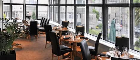 A modern dining area with large windows, black leather chairs, and a wooden table set for dining.