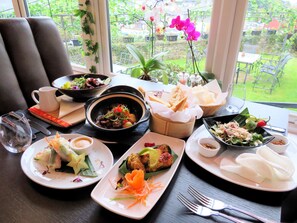 A table set with various dishes, including a bowl of soup, a plate of salad, and a plate of dumplings, with a view of a garden through the window. - Westberry Hotel (Bodmin)