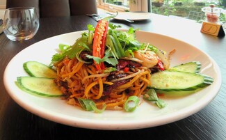 A plate of noodles with vegetables and shrimp, a glass of water, and a number 1 sign on a table.