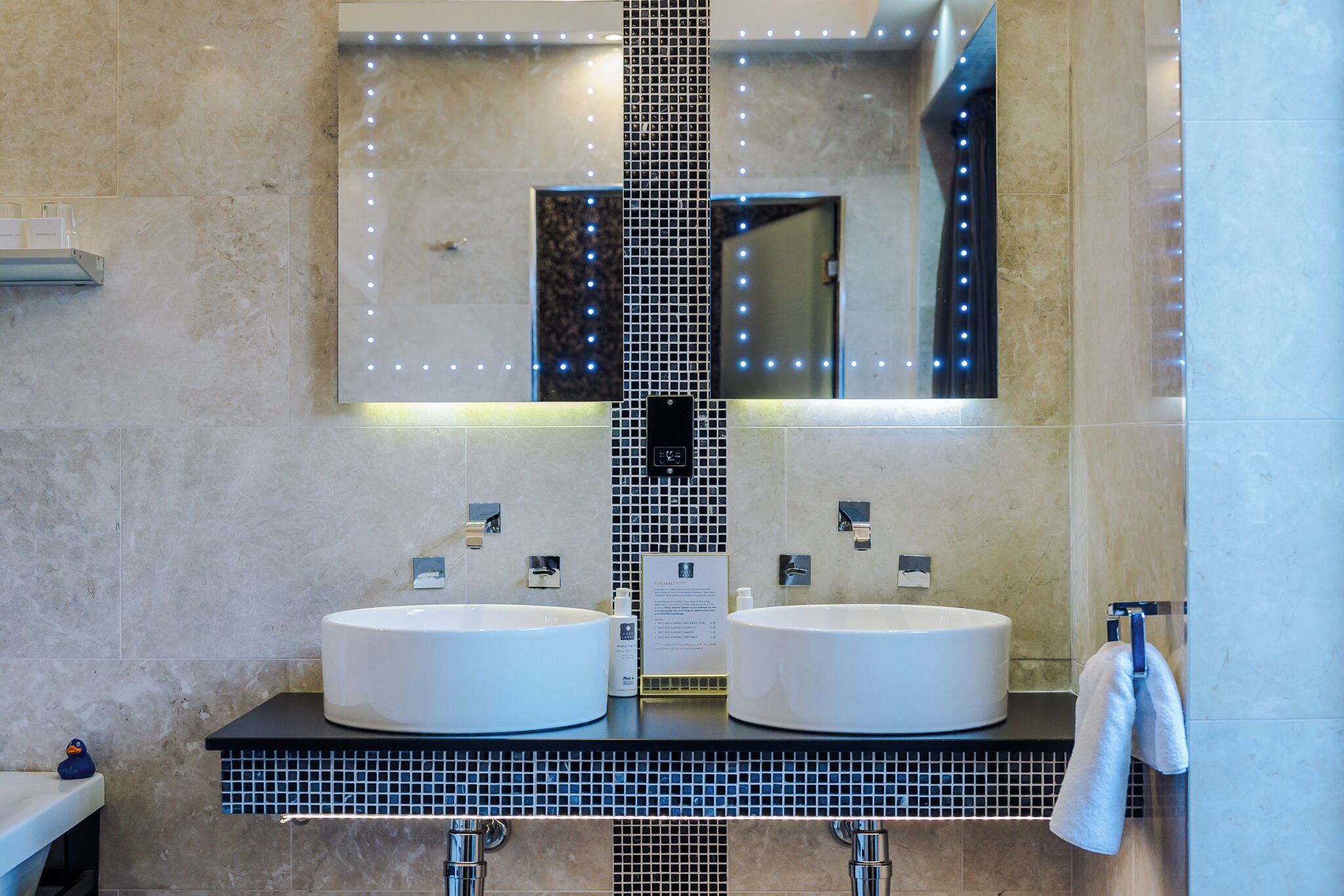 Un baño con dos lavamanos, un espejo con iluminación y un perchero para toallas.