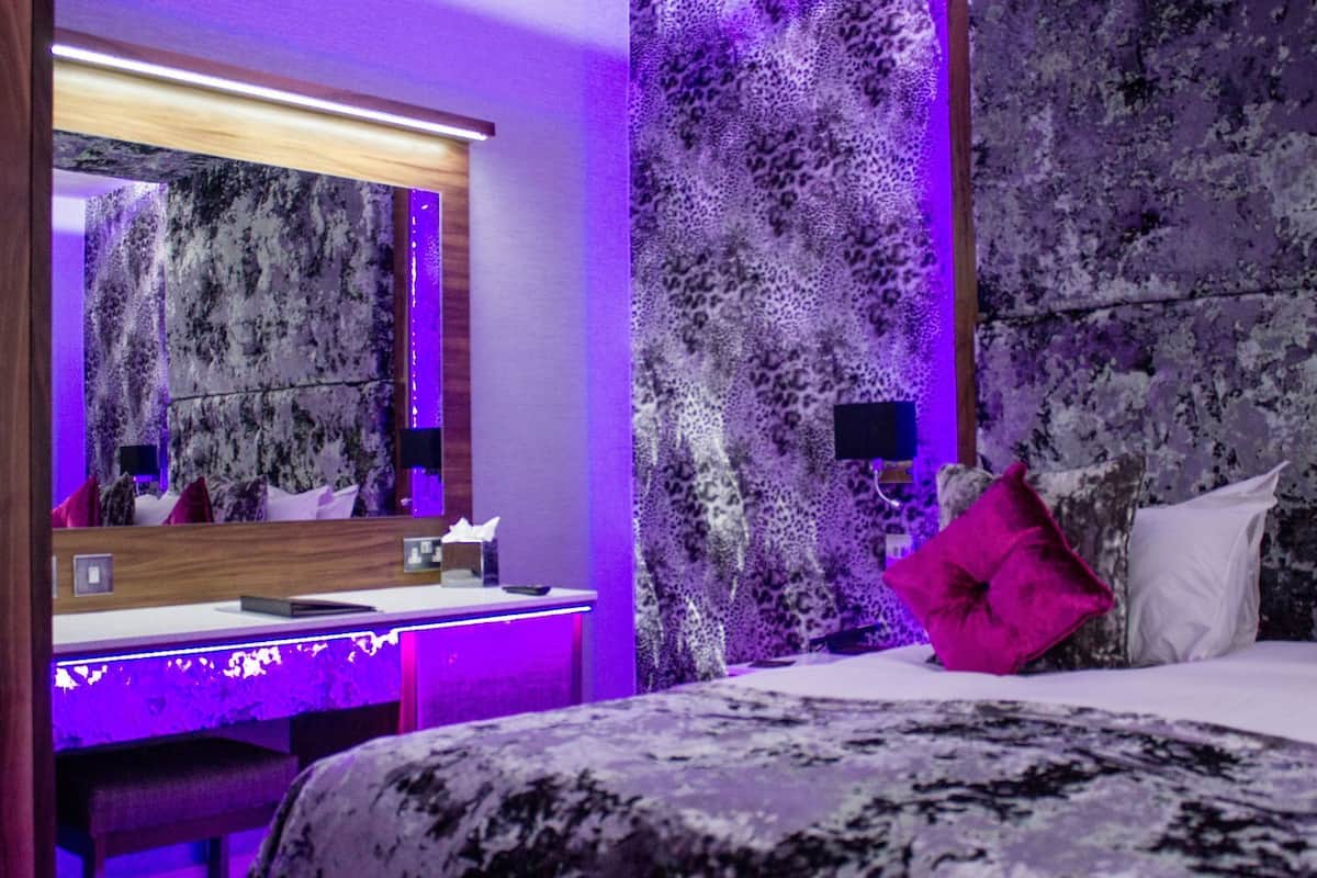 A modern bedroom with a large bed, a bedside table, a mirror, and a wall with a textured pattern.