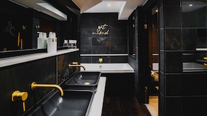 A modern bathroom with a black and gold color scheme, featuring a large mirror, a vanity with a sink, and a wall-mounted towel rack. - Cranleigh Boutique (Windermere)