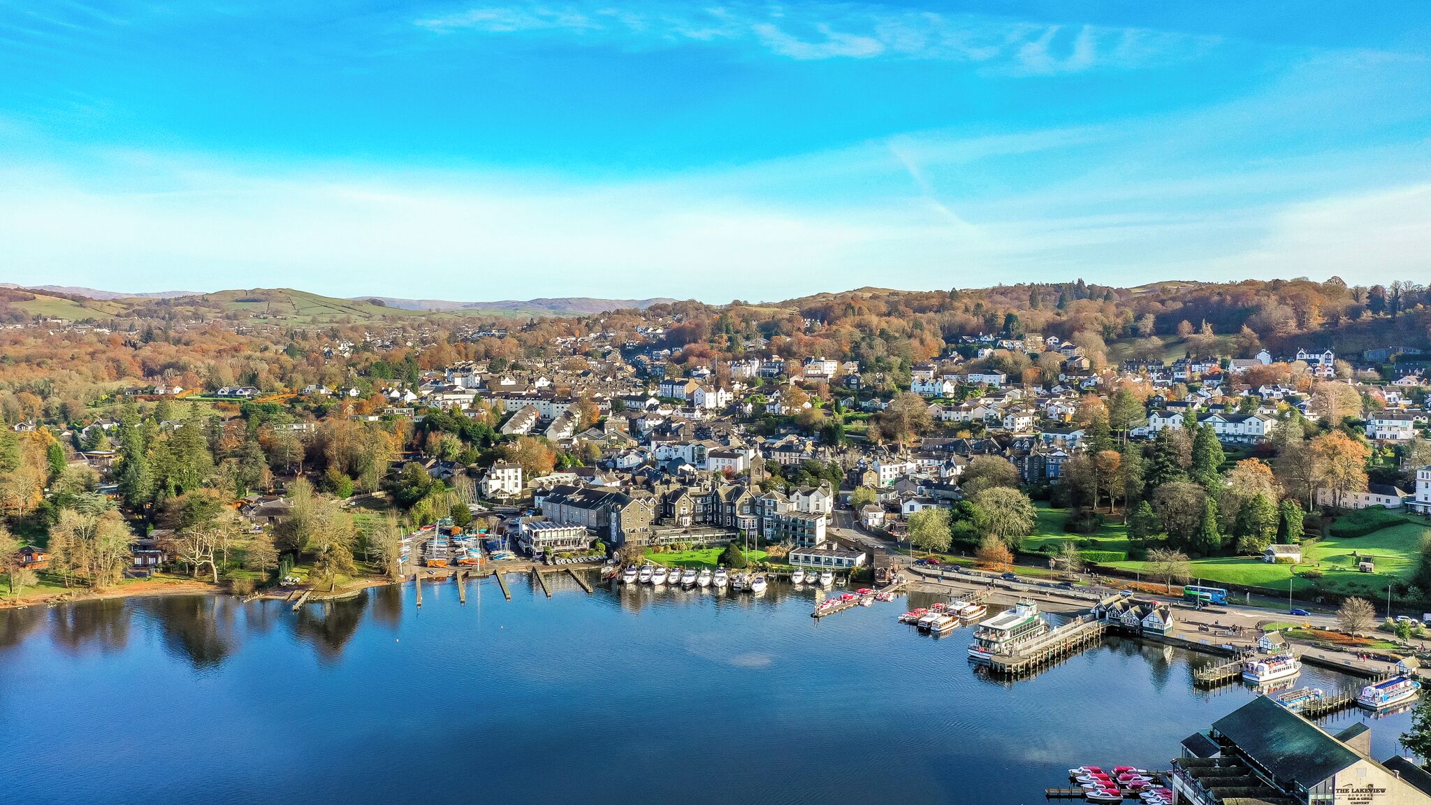 A lakeside town with residential buildings, a dock with boats, and a view of the surrounding hills.