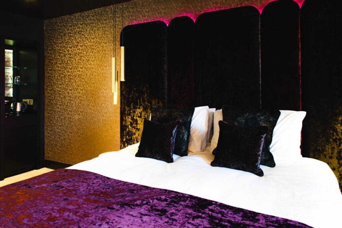 A bedroom with a large bed, a purple bedspread, and a textured wall.