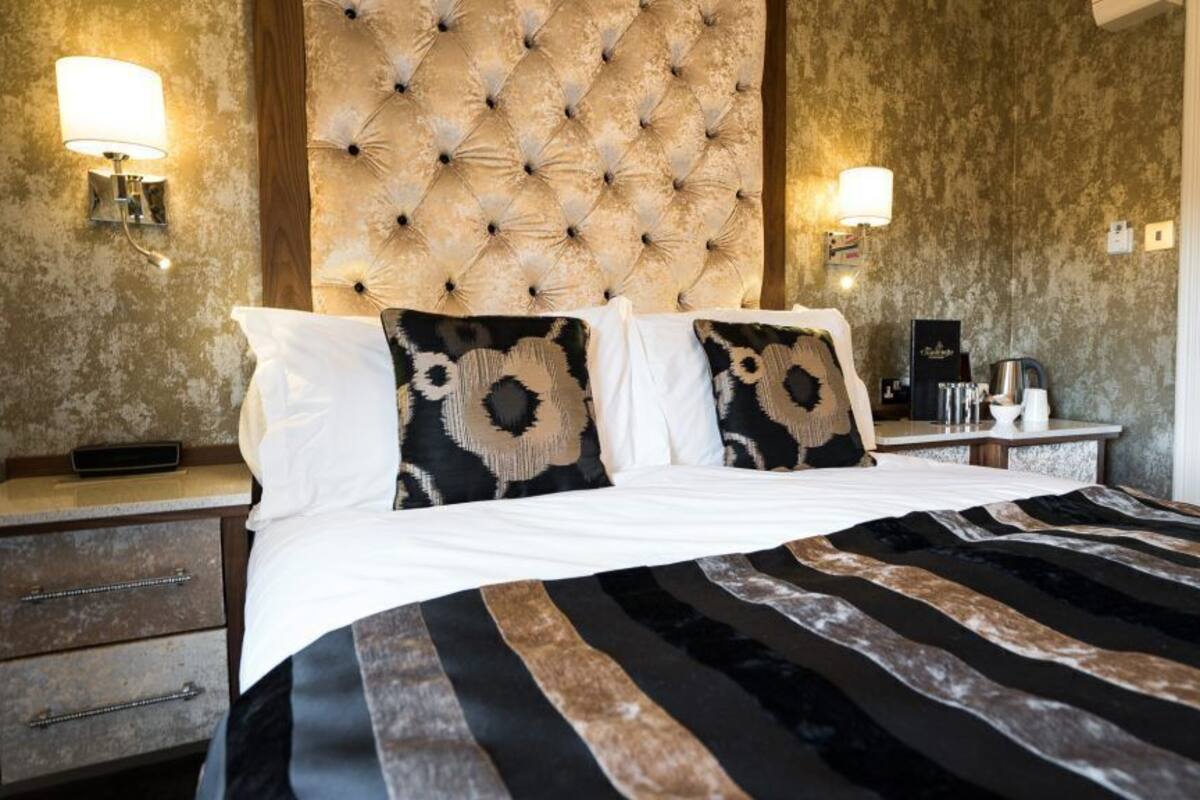 A bed with a striped bedspread, a tufted headboard, and two wall-mounted lamps.