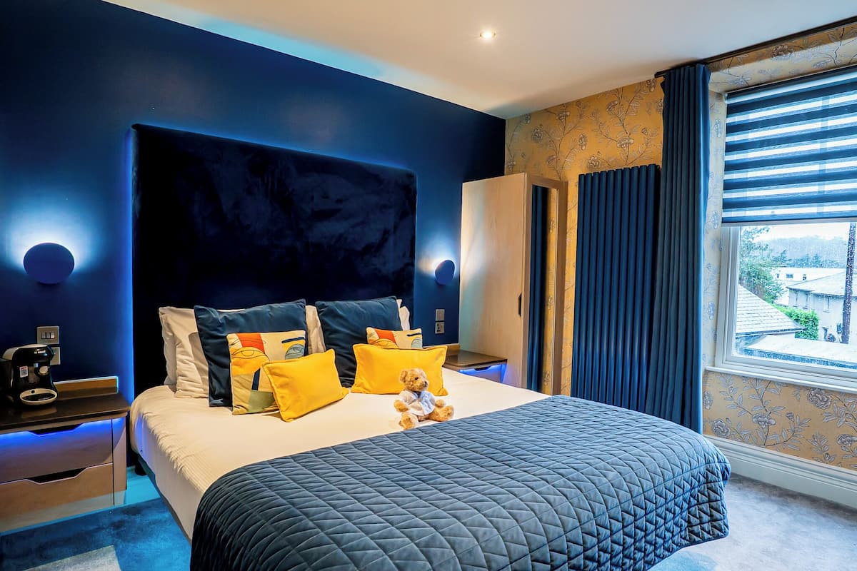 A modern bedroom with a large bed, dark blue walls, and a window with curtains.