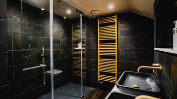 A modern bathroom with a glass shower enclosure, a wooden towel rack, and a black sink with gold fixtures.