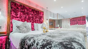 A modern bedroom with a large bed, a headboard with a textured pink panel, and a teddy bear on the bed. - Cranleigh Boutique (Windermere)