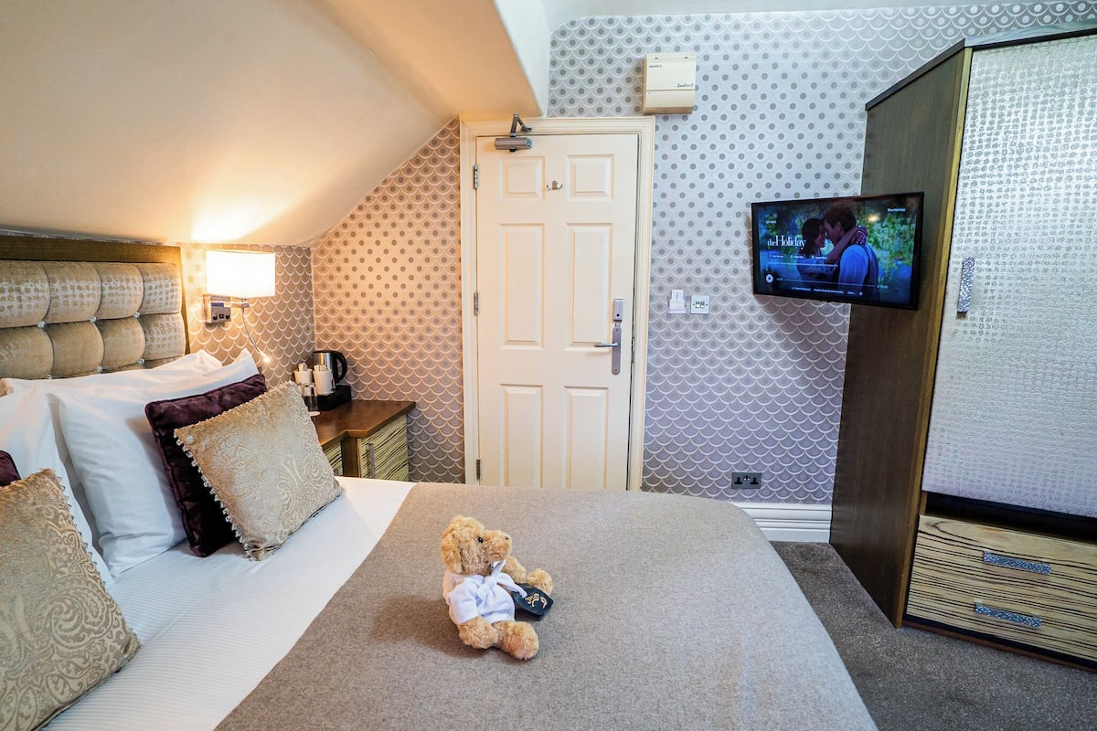 A hotel room with a bed, a teddy bear, a television, and a wardrobe.