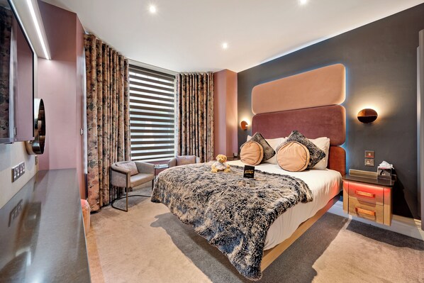 Un dormitorio moderno con una cama grande, mesitas de noche, una silla y un televisor.