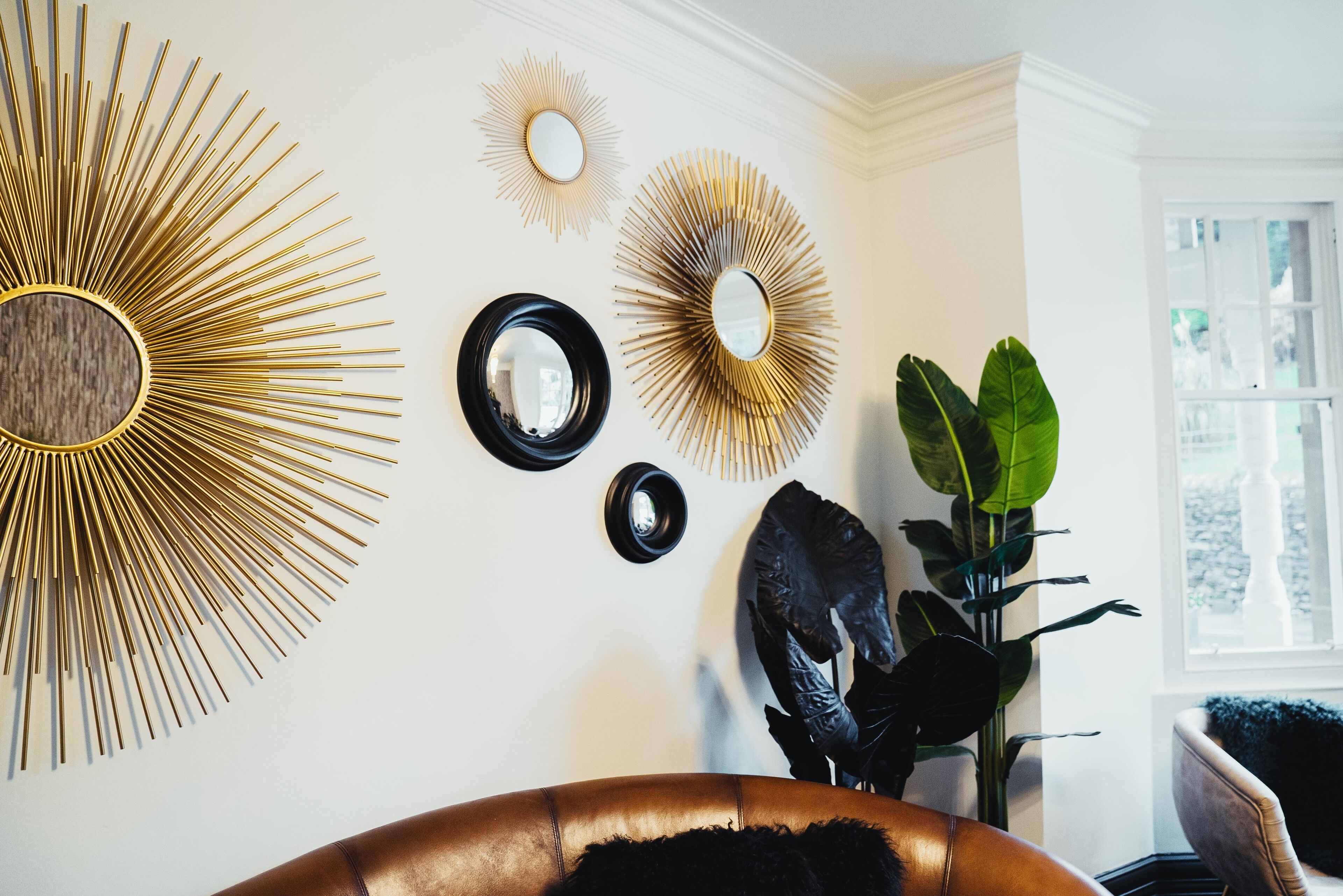 A room with a large sunburst mirror, smaller mirrors, and a plant.