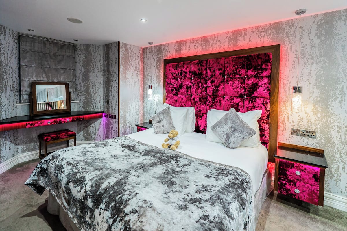 A modern bedroom with a large bed, a bedside table, a bench, and a headboard with a pink and black pattern.