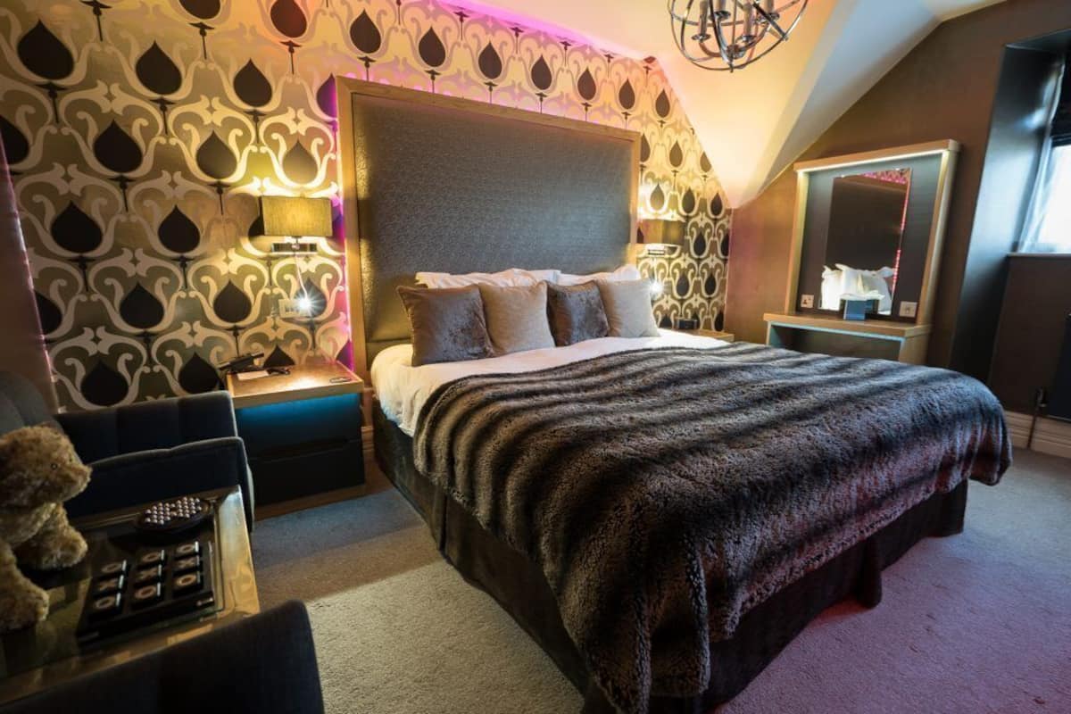 A bedroom with a large bed, a nightstand with a lamp, a dresser, and a mirror.
