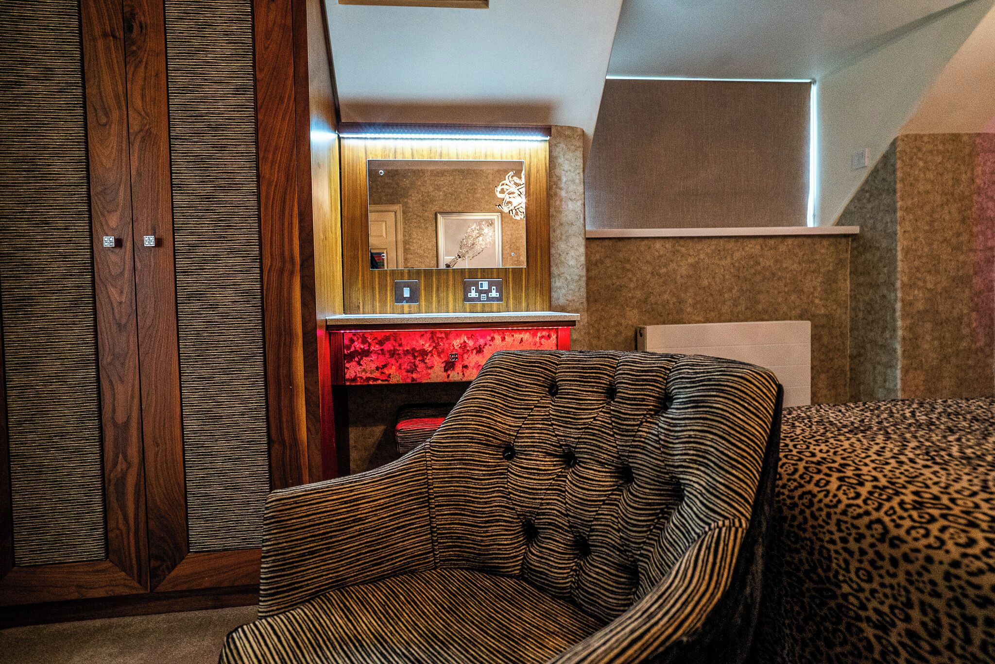 Una habitación con un sillón a rayas, un sofá estampado de leopardo y un espejo con marco rojo.