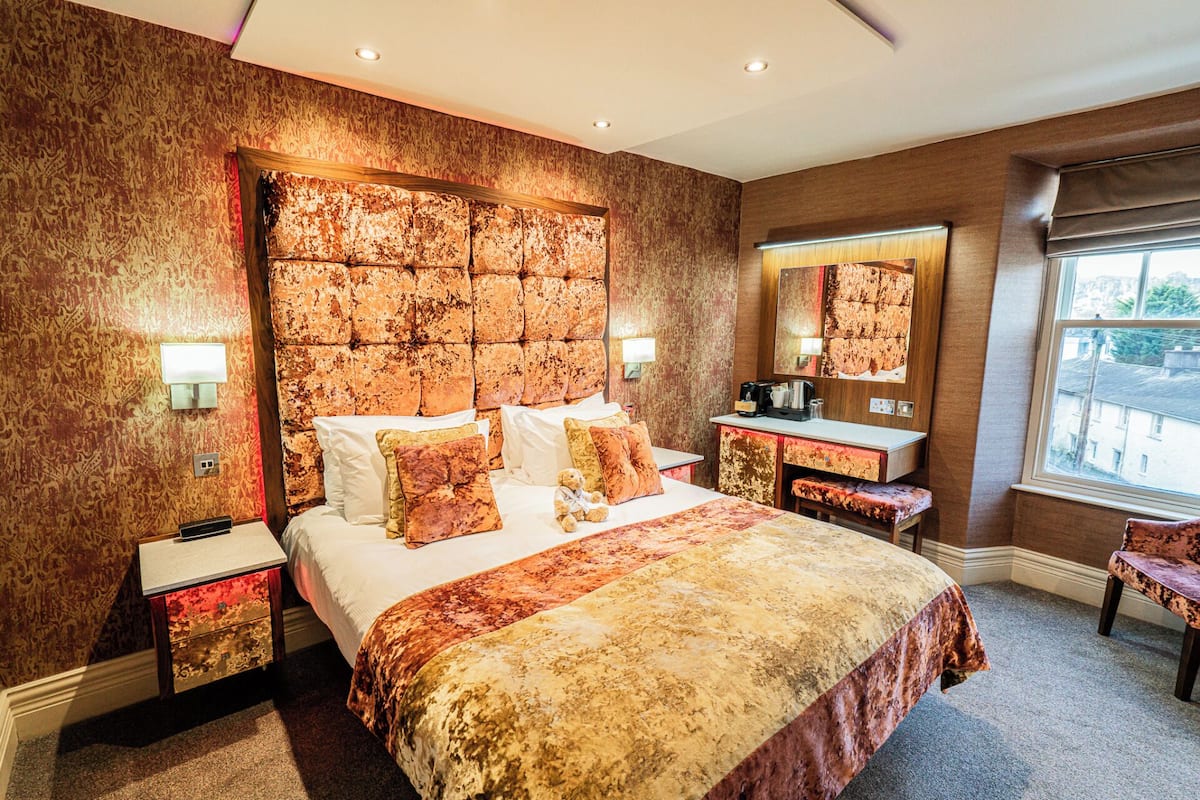 A hotel room with a large bed, a bedside table, a mirror, and a window.