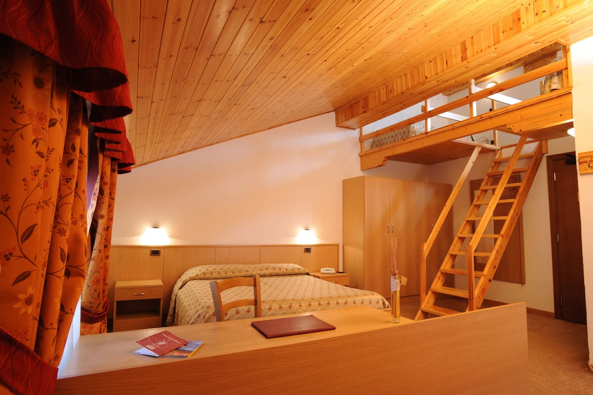 A wooden room with a bed, a desk, a ladder, and a small staircase.