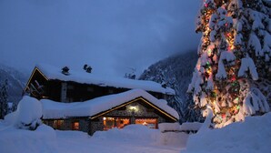 Una cabaña nevada con una entrada iluminada y un árbol de Navidad decorado.