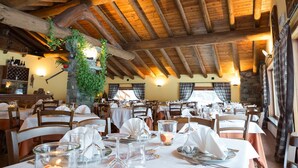 Un restaurante con vigas de madera y paredes de piedra, mesas preparadas para comer y una planta colgante.
