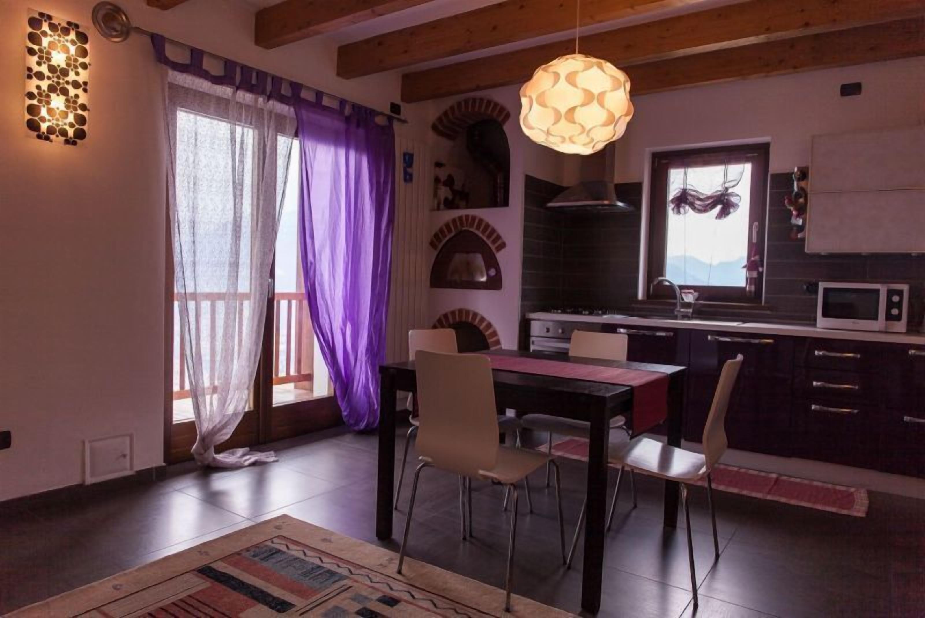 Un comedor con mesa y sillas, una cocina con microondas, y un ventanal con vistas a montañas.