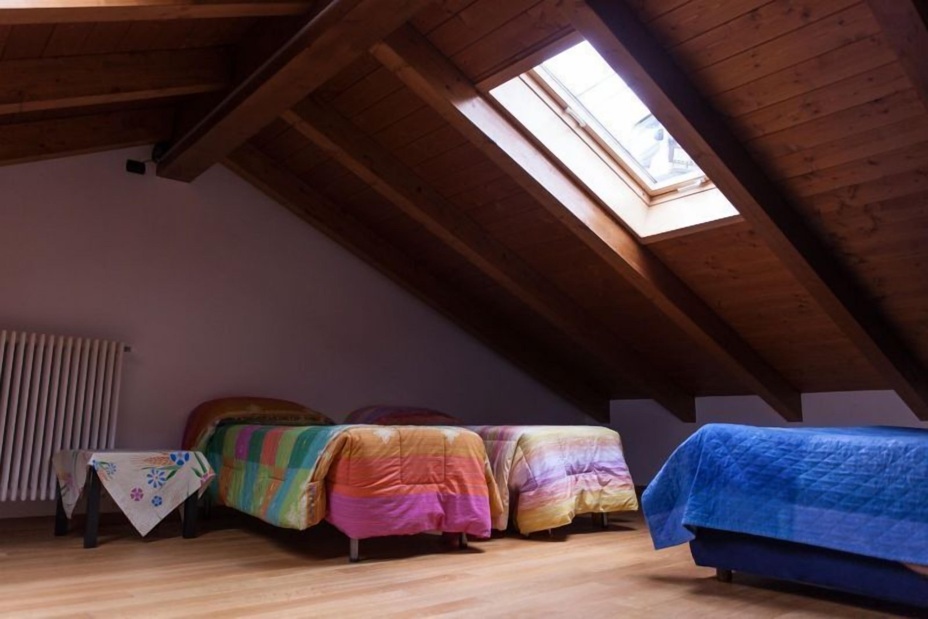 Una camera del dormitorio con tre letti, una finestra a soffitto, un termosifone e un piccolo tavolo con una tovaglia fiorita.
