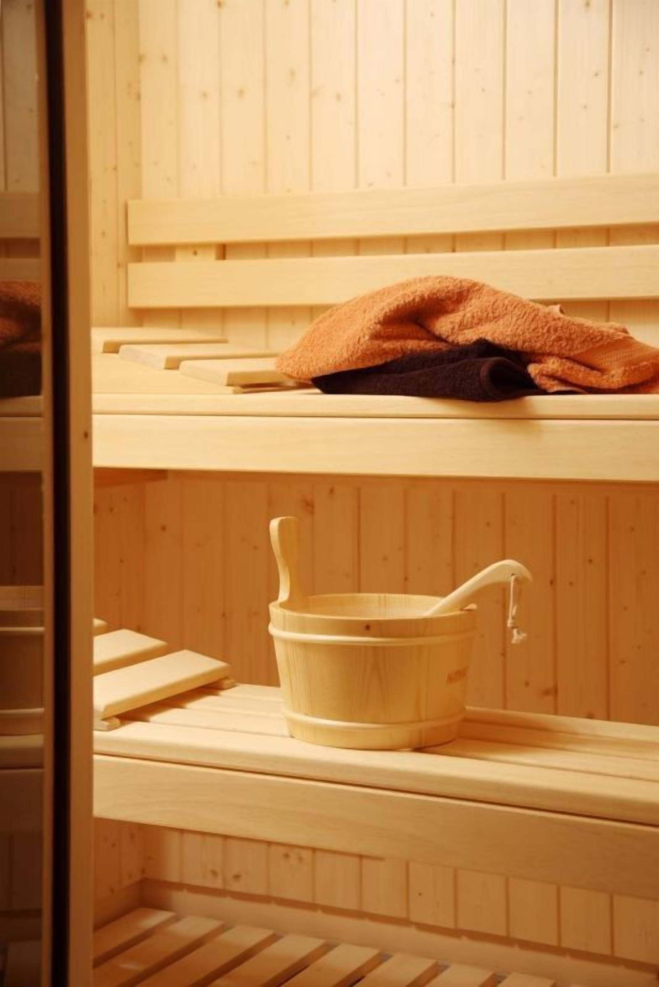 Un sauna en bois, avec des bancs et un seau en bois muni d’un robinet.