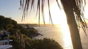 A coastal view with a sunset, palm trees, and outdoor seating.