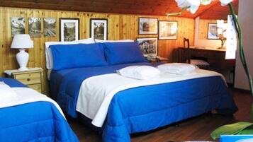 A room with two beds, wooden walls, framed pictures, a desk, and a lamp.