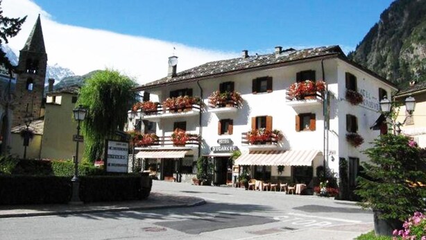 A building with multiple balconies, a sign indicating a hotel, and a mountainous backdrop. - Hotel Bucaneve (Pre-Saint-Didier)