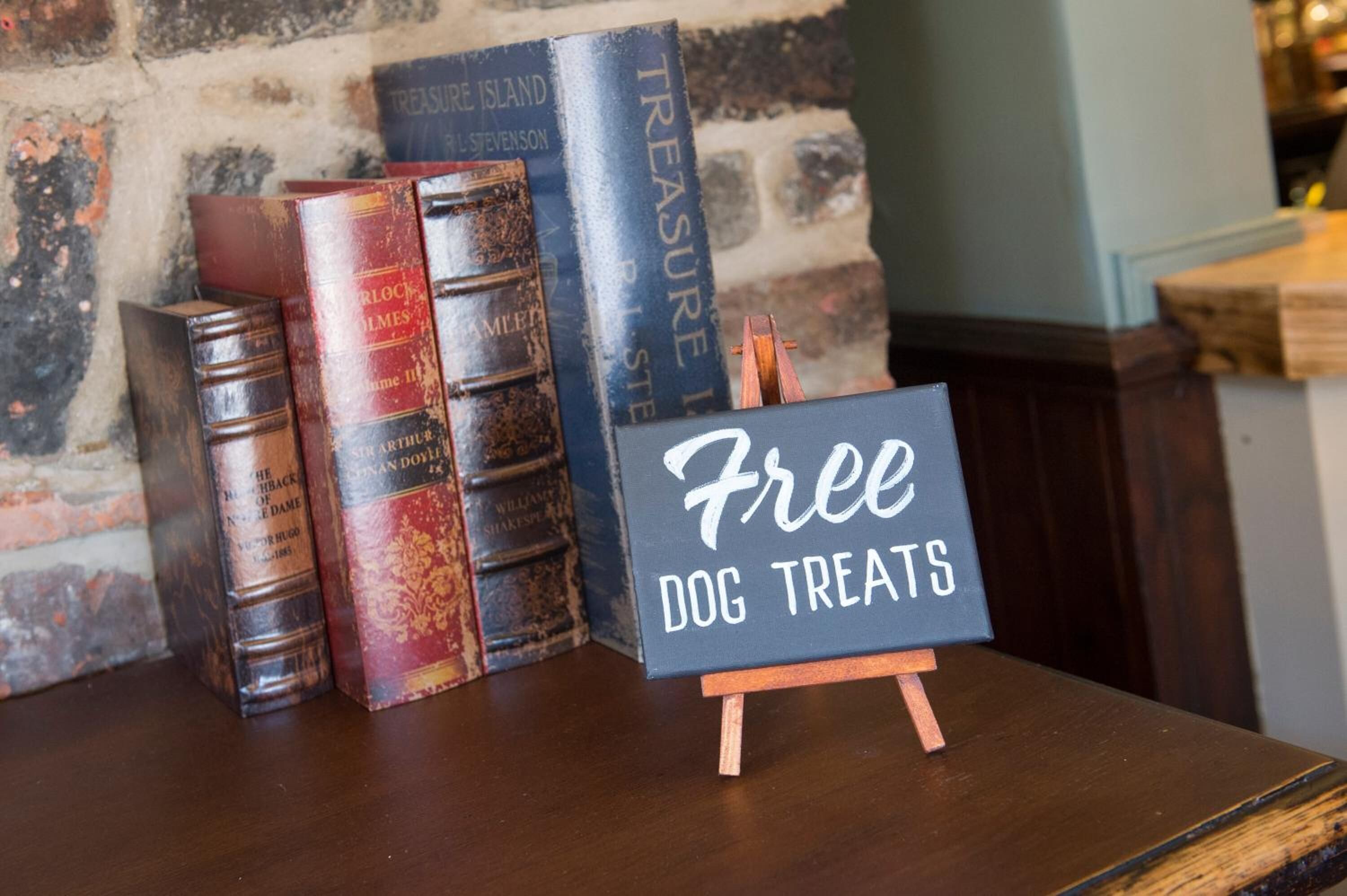 Un tavolo di legno con un cartello che offre dolcetti gratuiti per cani, circondato da libri d'epoca.