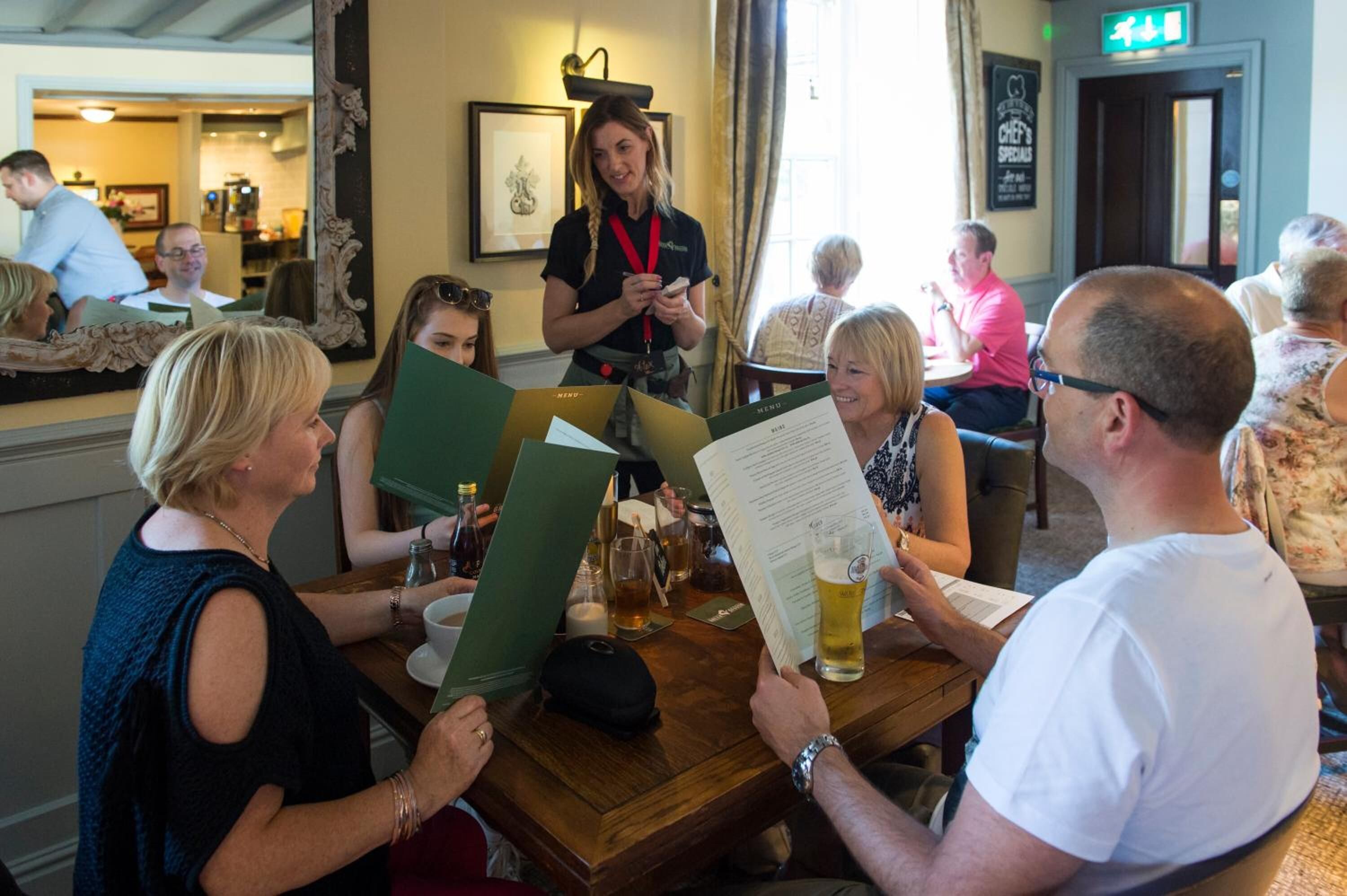 A group of people seated at a wooden table in a restaurant, reading menus.
