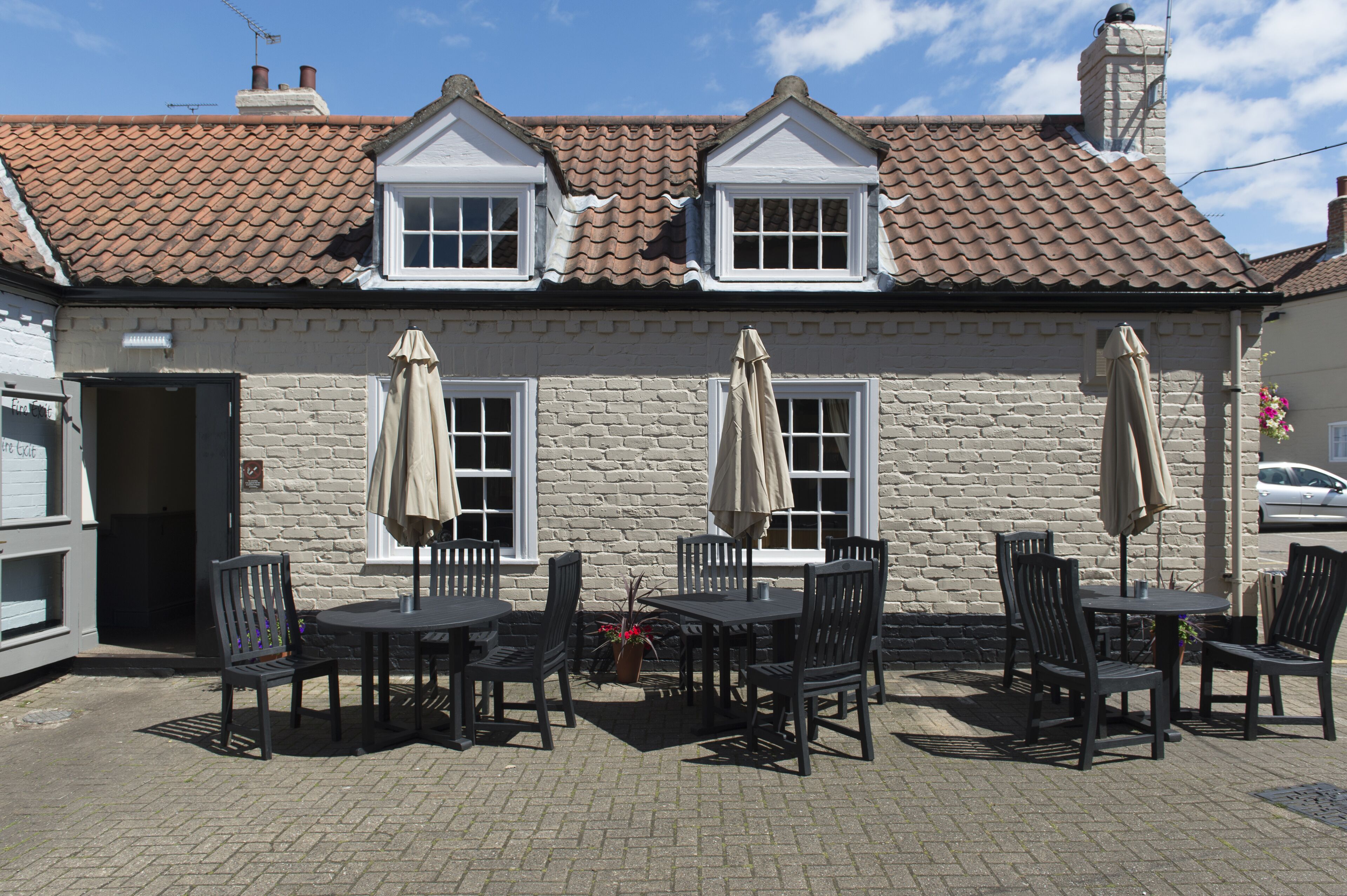 A building with a tiled roof, a brick facade, and a set of outdoor tables and chairs.