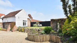A white building with a red-tiled roof, surrounded by a garden with a wooden raised bed and a stone wall.